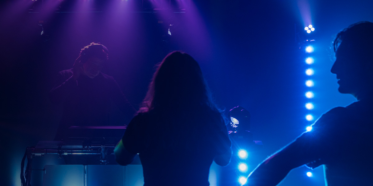 2 People Partying In Front Of The Dj With Lighting Effect On Stage